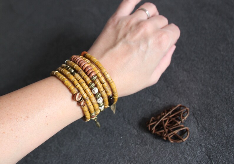 May include: A stack of yellow, brown, and white beaded bracelets on a person's wrist. The bracelets are made of natural materials and have a rustic, bohemian style.