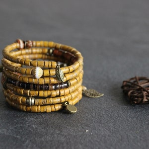 May include: A multi-strand bracelet made of yellow wooden beads with brown and white accents. The bracelet has several metal charms, including leaves and circles.