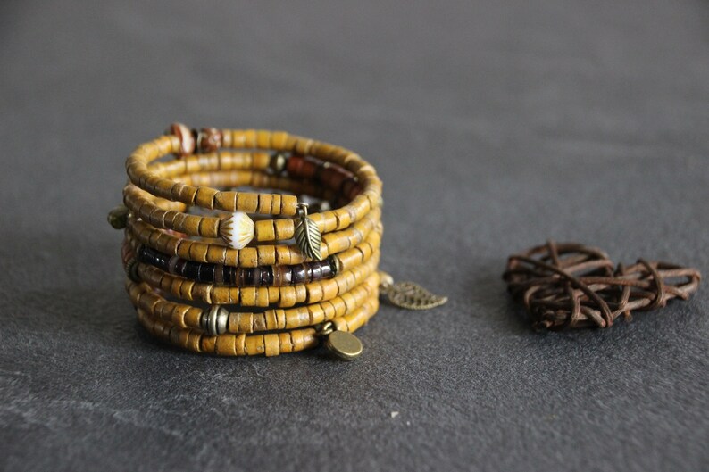May include: A multi-strand bracelet made of yellow wooden beads with brown and white accents. The bracelet has several metal charms, including leaves and circles.