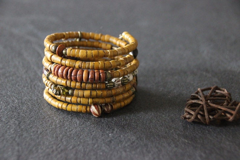 May include: A multi-layered bracelet made of yellow, brown, and white beads. The bracelet is wrapped around itself several times, creating a thick, textured look.