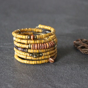 May include: A multi-strand bracelet made of yellow, brown, and orange wooden beads. The bracelet is wrapped around itself to create a thick, layered look.