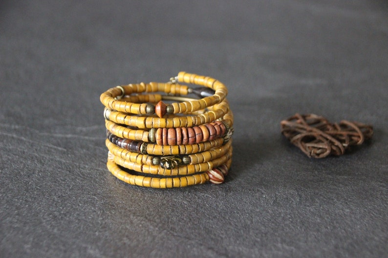 May include: A multi-strand bracelet made of yellow, brown, and orange wooden beads. The bracelet is wrapped around itself to create a thick, layered look.