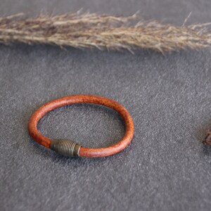 Puede incluir: Un brazalete de cuero marr&oacute;n con un cierre de metal plateado.