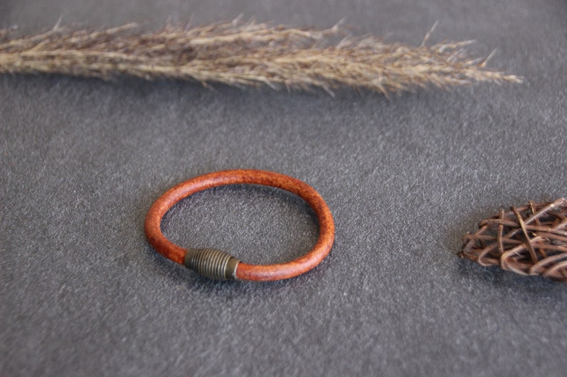 Puede incluir: Un brazalete de cuero marr&oacute;n con un cierre de metal plateado.