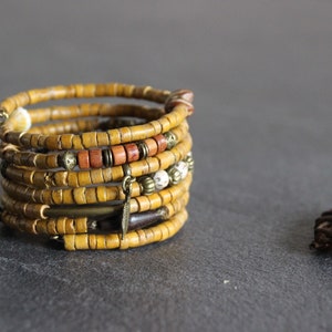 May include: A multi-strand bracelet made of yellow wood beads with brown and white accents. The bracelet has several metal charms, including a feather and a small disc.
