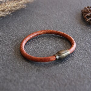 Puede incluir: Un brazalete de cuero marr&oacute;n con un cierre de lat&oacute;n.