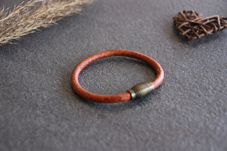 Puede incluir: Un brazalete de cuero marr&oacute;n con un cierre de lat&oacute;n.