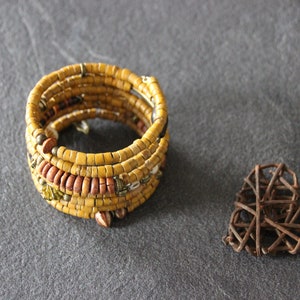 May include: A yellow and brown beaded bracelet with a woven heart made of brown twigs.