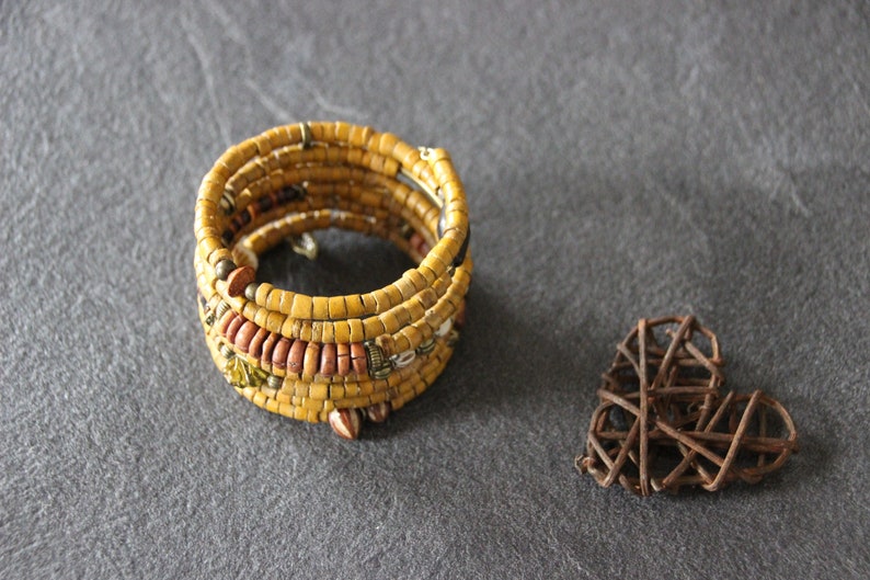 May include: A yellow and brown beaded bracelet with a woven heart made of brown twigs.