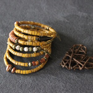 May include: A stack of yellow, brown, and white beaded bracelets with metal accents. The bracelets are stacked on a gray surface.