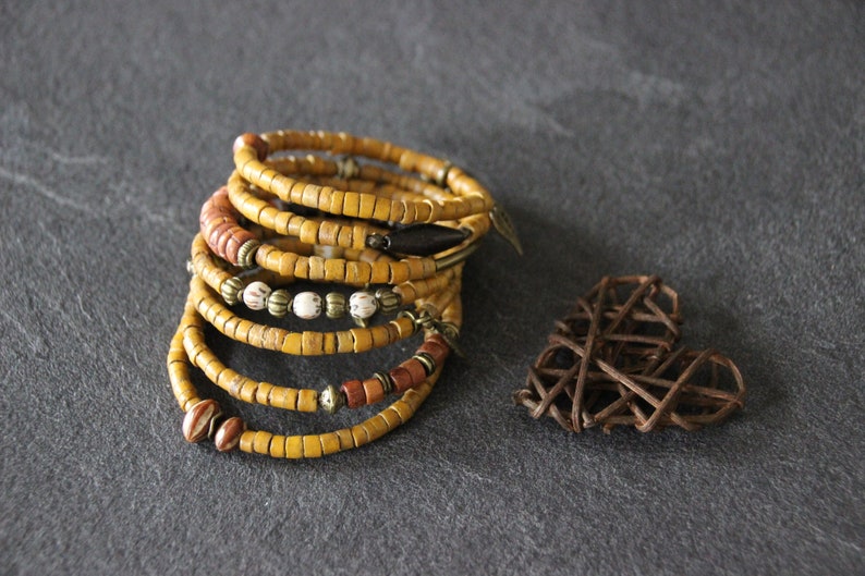 May include: A stack of yellow, brown, and white beaded bracelets with metal accents. The bracelets are stacked on a gray surface.