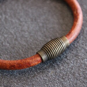 Puede incluir: Un brazalete de cuero marr&oacute;n con un cierre magn&eacute;tico de lat&oacute;n. El brazalete est&aacute; hecho de una sola pieza de cuero y tiene un dise&ntilde;o simple y minimalista.