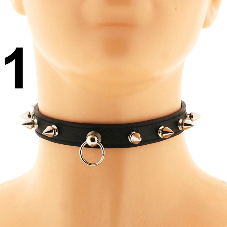 Crafted from sleek black faux leather, this choker showcases a distinctive hanging ring and spikes, secured with a buckle closure. Its edgy design exudes a stylish punk or rock aesthetic