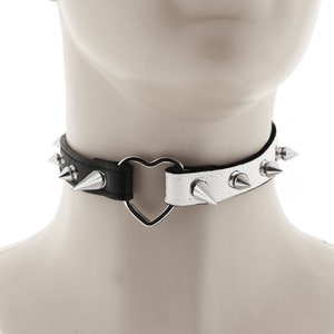 This rock punk necklace choker collar is crafted from vegan faux leather in white and black. It features a heart ring and a spiked adjustable buckle closure.