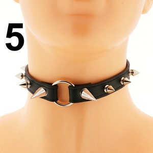 The choker necklace showcases a ring and spikes, complemented by a buckle closure, all crafted from sleek black faux leather. This exquisite accessory exudes a fashionable punk or rock aesthetic.