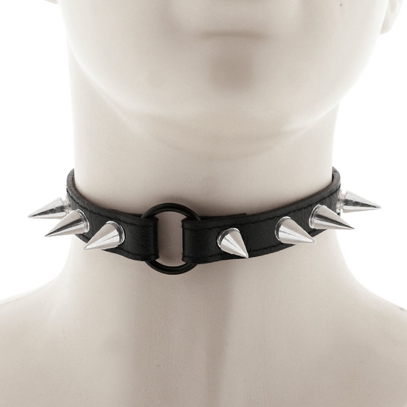 The choker has a ring, spikes, and a buckle closure, all made of black faux leather for a punk or rock style.