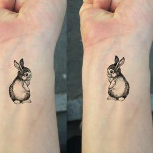 May include: A black and white line drawing of a rabbit on a person's wrist.