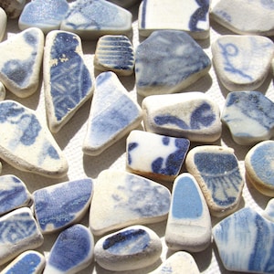 May include: An assortment of blue and white ceramic fragments, displaying diverse patterns and forms. The pieces, of varying sizes, have a worn look, indicating they are remnants of broken pottery.