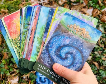 May include: A deck of oracle cards with a blue, green, and white watercolor design. The card in the front reads "The Great Web" with the words "Interconnection, Kinship, Symbiosis" below.