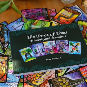 May include: A collection of colorful tarot cards and a book titled "The Tarot of Trees: Artwork and Meanings" by Dana O'Driscoll. The cards feature vibrant illustrations of trees and nature scenes, with a dark green book cover.
