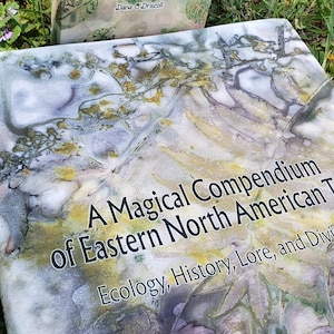 May include: A book titled "A Magical Compendium of Eastern North American Trees: Ecology, History, Lore, and Divination" by Dana Driscoll. The cover features a watercolour-style design of leaves in shades of green, brown, and purple.