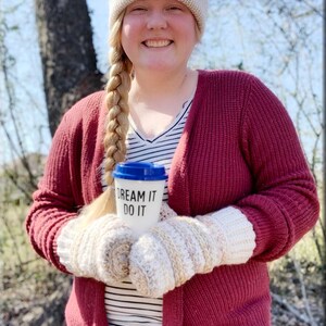 K&ouml;nnte beinhalten: Eine Frau tr&auml;gt einen roten Cardigan, ein wei&szlig;-schwarz gestreiftes Hemd, eine wei&szlig;e M&uuml;tze mit einem braunen Aufn&auml;her, auf dem "Wild Thing" steht, und wei&szlig;e gestrickte Fingerhandschuhe. Sie h&auml;lt eine wei&szlig;e Reise-Thermoskanne mit blauem Deckel, auf der "Dream It Do It" steht.