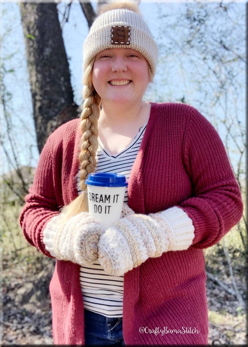 K&ouml;nnte beinhalten: Eine Frau tr&auml;gt einen roten Cardigan, ein wei&szlig;-schwarz gestreiftes Hemd, eine wei&szlig;e M&uuml;tze mit einem braunen Aufn&auml;her, auf dem "Wild Thing" steht, und wei&szlig;e gestrickte Fingerhandschuhe. Sie h&auml;lt eine wei&szlig;e Reise-Thermoskanne mit blauem Deckel, auf der "Dream It Do It" steht.