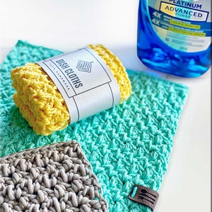 May include: Three crocheted dishcloths in yellow, teal and grey. The yellow dishcloth has a label that reads "Dish Cloths 100% Handmade".