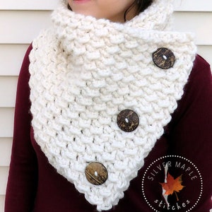May include: White crocheted cowl with three wooden buttons. The cowl is folded over and worn around the neck. The text "Silver Maple Stitches" is visible in the lower right corner of the image.