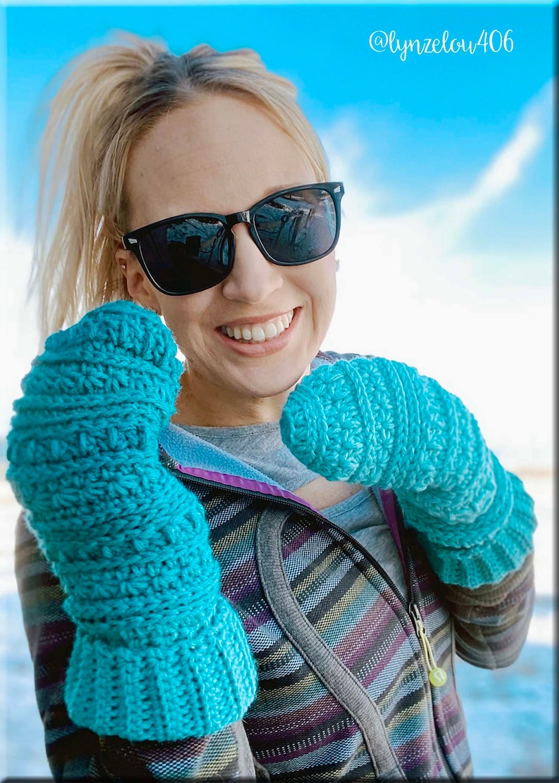 K&ouml;nnte beinhalten: Eine Frau mit Sonnenbrille und einer gestreiften Jacke h&auml;lt ein Paar tealblaue, geh&auml;kelte Fingerhandschuhe. Die Handschuhe haben ein strukturiertes Stichmuster. Das Bild enth&auml;lt den Text "@lynzelow406".