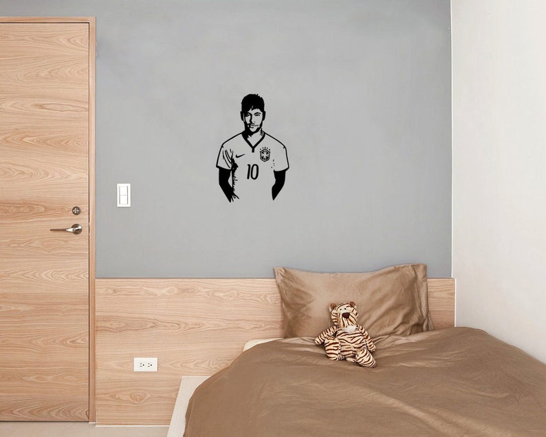 K&ouml;nnte beinhalten: Eine schwarz-wei&szlig;e Silhouette eines Fu&szlig;ballspielers, der ein Trikot mit der Nummer 10 tr&auml;gt. Der Spieler steht an einer grauen Wand mit einem Holz-Kopfteil und einer braunen Bettdecke dahinter.