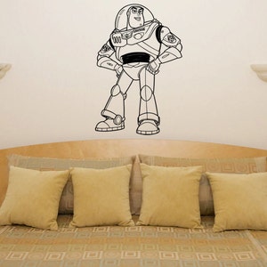 Puede incluir: Pegatina de pared de arte de l&iacute;nea en blanco y negro de Buzz Lightyear de la franquicia de pel&iacute;culas Toy Story. La pegatina est&aacute; en una pared blanca sobre una cama con ropa de cama de color canela.