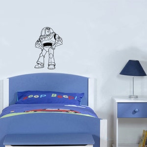 Puede incluir: Un contorno en blanco y negro de Buzz Lightyear de la serie de pel&iacute;culas Toy Story en una pared blanca sobre una cama azul con una almohada que dice "&iexcl;Bip Bip!"