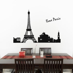May include: Black and white silhouette wall decal of the Eiffel Tower and Parisian cityscape with the text "I Love Paris". The decal is displayed on a white wall above a dark wood dining table with six chairs.