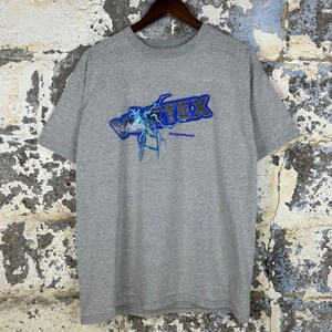 May include: A gray t-shirt featuring the word "VORTEX" in blue and white, with a lightning bolt design. Below the word "VORTEX" is the text "Kings Island". The shirt is hanging on a wooden hanger.