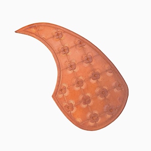 May include: A curved, reddish-brown leather guitar pickguard with a floral pattern. The pickguard has a grid-like design with embossed flower shapes. The edges are rounded, and the overall shape is reminiscent of a teardrop.