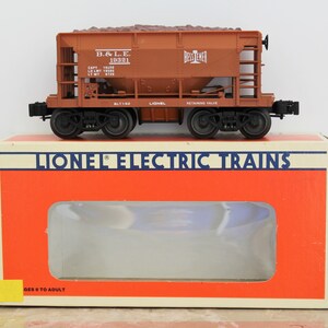 May include: A brown and tan Lionel model train car with the text "B.& L.E. 19321" and "BESSEMER" printed on the side. The car is labeled "BLT1-92" and "LIONEL". The car is on a red box with the text "LIONEL ELECTRIC TRAINS" printed on the top.