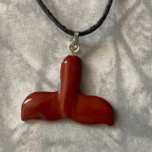 Op de afbeelding: Een rode edelsteen walstaart hanger aan een zwart koordsnoer.