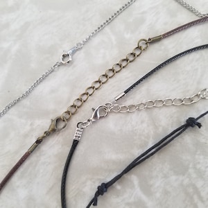 May include: A selection of necklace chains and cords with clasps and extenders. The chains are silver, and the cords are brown and black. The extenders are made of silver and bronze-coloured metal. The image displays different styles of jewellery components.