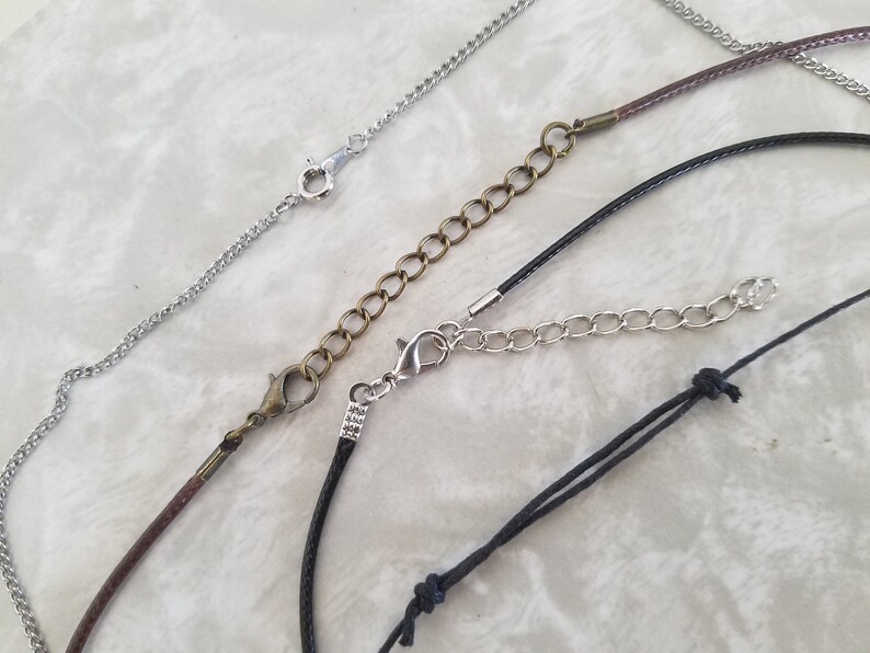 May include: A selection of necklace chains and cords with clasps and extenders. The chains are silver, and the cords are brown and black. The extenders are made of silver and bronze-coloured metal. The image displays different styles of jewellery components.