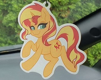 Può includere: Un cavallo di cartone animato giallo e arancione con criniera e coda rosse. Il cavallo ha un simbolo del sole sul fianco. Il cavallo è un deodorante per auto.