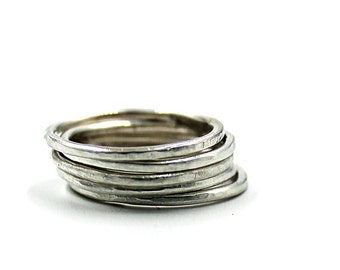 May include: A stack of six silver rings, each with a hammered texture.