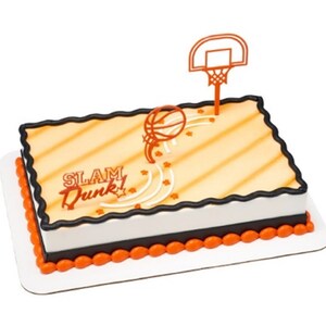 Peut inclure: Un g&acirc;teau carr&eacute; d&eacute;cor&eacute; d'un motif de terrain de basket-ball, d'un ballon de basket et d'un panier de basket. Le g&acirc;teau est glac&eacute; en orange et blanc avec une bordure noire et les mots "SLAM Dunk!" en orange.