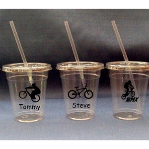 May include: Four clear plastic cups with straws and black and white graphics of people riding bicycles. The cups are labeled "Tommy", "Steve", "Carrie", and "BMX".