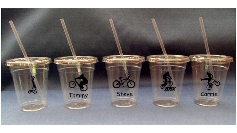 May include: Four clear plastic cups with straws and black and white graphics of people riding bicycles. The cups are labeled "Tommy", "Steve", "Carrie", and "BMX".