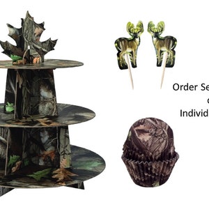 May include: Three-tiered cardboard cake stand with a camouflage pattern. The top tier has a green leaf design. Two deer cupcake toppers and a camouflage cupcake liner are also included. Order Set as Shown or Individual pieces.