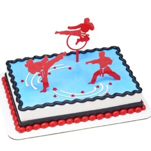 May include: A blue and white cake decorated with red karate figures. The cake is on a white cake board with a red border.