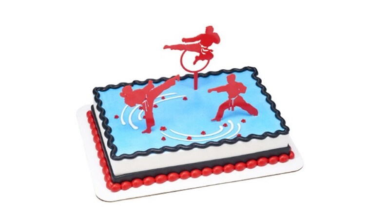 May include: A blue and white cake decorated with red karate figures. The cake is on a white cake board with a red border.