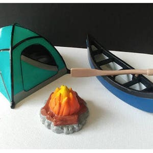 May include: A blue and green camping tent, a blue canoe with a wooden paddle, and a small orange and yellow campfire.