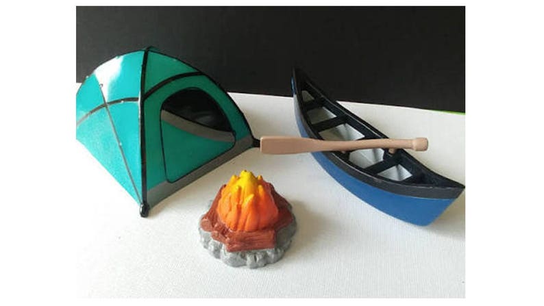 May include: A blue and green camping tent, a blue canoe with a wooden paddle, and a small orange and yellow campfire.